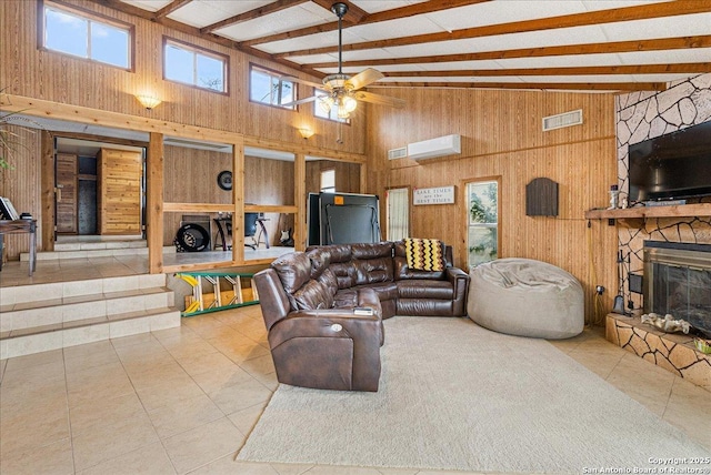 tiled living room with vaulted ceiling with beams, a stone fireplace, ceiling fan, a wall mounted AC, and wood walls