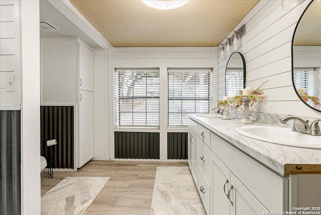 bathroom with a textured ceiling, vanity, hardwood / wood-style floors, and wood walls