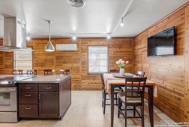 kitchen featuring dark brown cabinets, hanging light fixtures, stainless steel electric range oven, island exhaust hood, and wood walls