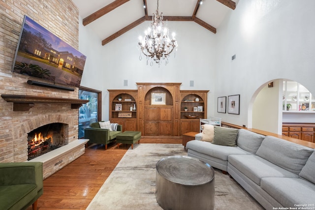 living room with hardwood / wood-style flooring, beam ceiling, high vaulted ceiling, a large fireplace, and a chandelier