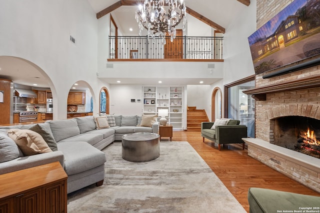 living room with built in shelves, a fireplace, beamed ceiling, light wood-type flooring, and an inviting chandelier