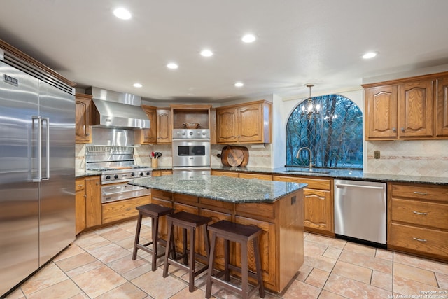 kitchen featuring hanging light fixtures, wall chimney exhaust hood, stainless steel appliances, a center island, and sink