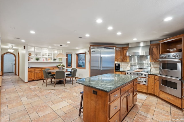 kitchen featuring appliances with stainless steel finishes, pendant lighting, a kitchen island, wall chimney exhaust hood, and decorative backsplash