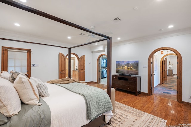 bedroom featuring light wood-type flooring, ornamental molding, and a walk in closet