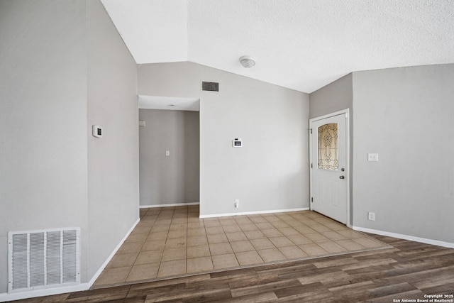 spare room with hardwood / wood-style flooring, vaulted ceiling, and a textured ceiling