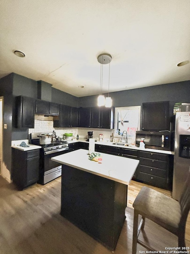 kitchen featuring appliances with stainless steel finishes, sink, light hardwood / wood-style flooring, a center island, and decorative light fixtures