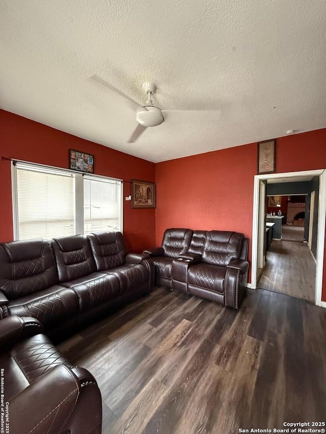 living room featuring ceiling fan, dark wood-type flooring, and a textured ceiling