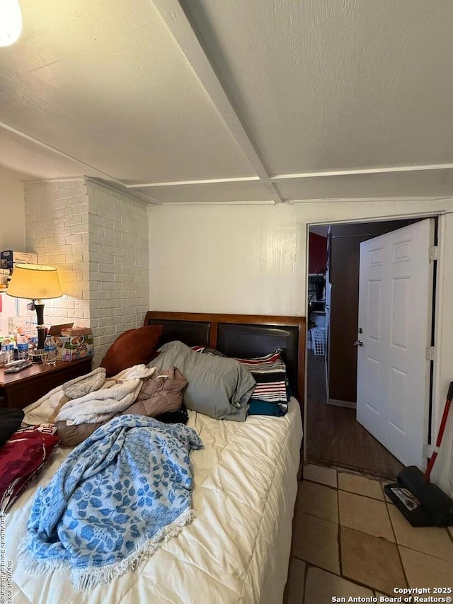 bedroom featuring tile patterned flooring, brick wall, and a textured ceiling