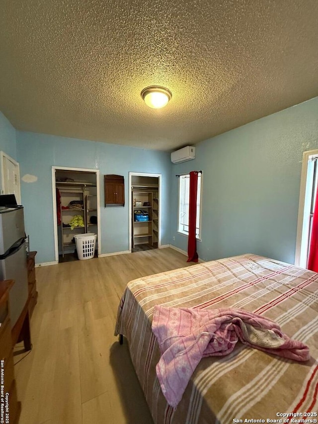 bedroom featuring light wood-type flooring, a wall mounted AC, and a textured ceiling