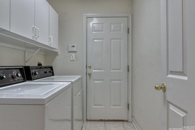 clothes washing area with washing machine and clothes dryer, light tile patterned floors, and cabinets