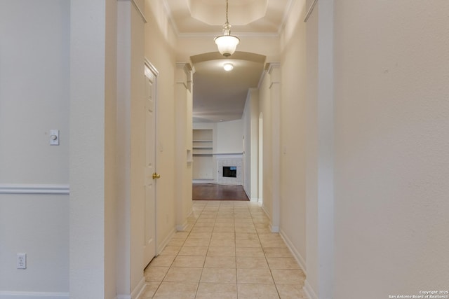 hallway with light tile patterned flooring, crown molding, and a raised ceiling