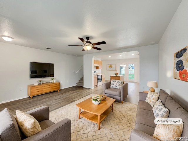 living area with arched walkways, visible vents, ceiling fan, wood finished floors, and stairs