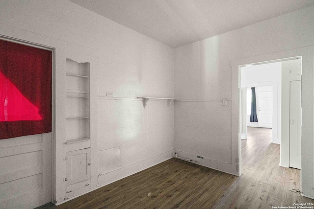 spare room featuring built in shelves and wood-type flooring