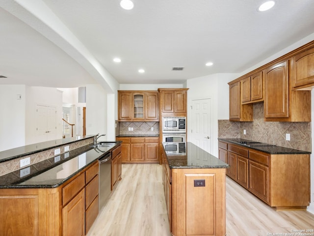 kitchen with sink, appliances with stainless steel finishes, dark stone countertops, and a center island