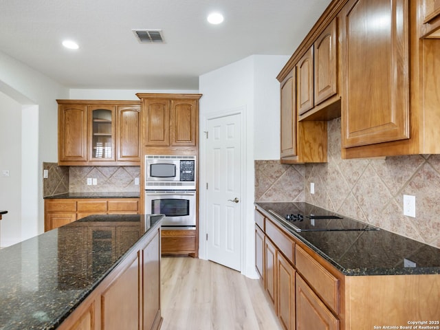 kitchen with appliances with stainless steel finishes, light hardwood / wood-style flooring, dark stone countertops, and decorative backsplash