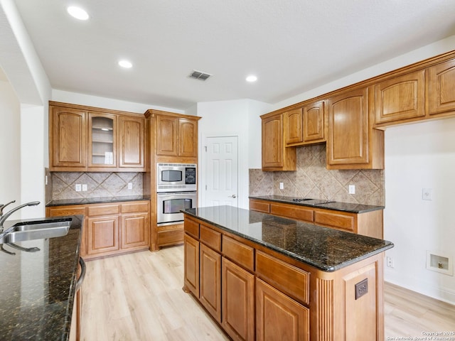 kitchen featuring dark stone countertops, a center island, light hardwood / wood-style floors, sink, and appliances with stainless steel finishes