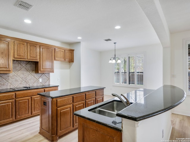 kitchen featuring light wood-type flooring, a kitchen island with sink, sink, backsplash, and pendant lighting