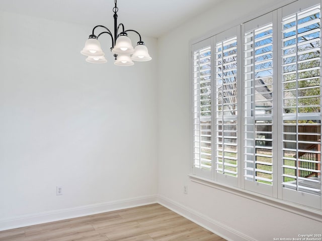 unfurnished room featuring a notable chandelier, plenty of natural light, and light hardwood / wood-style flooring