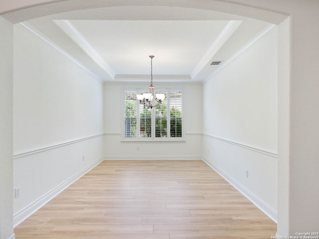 unfurnished dining area featuring a tray ceiling, crown molding, light wood-type flooring, and a notable chandelier