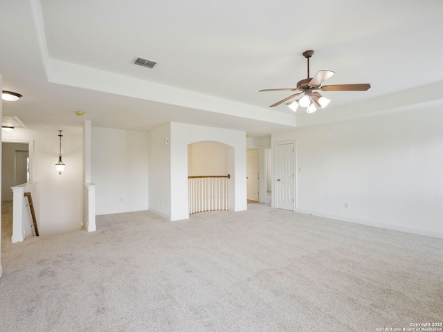 carpeted spare room featuring a raised ceiling and ceiling fan