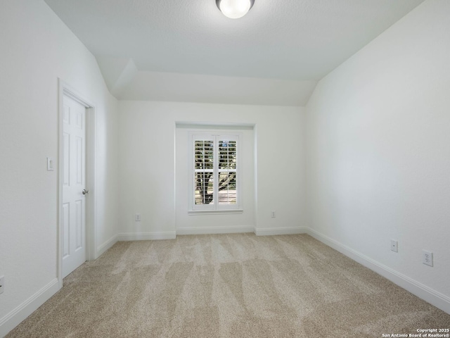 empty room with vaulted ceiling and light colored carpet