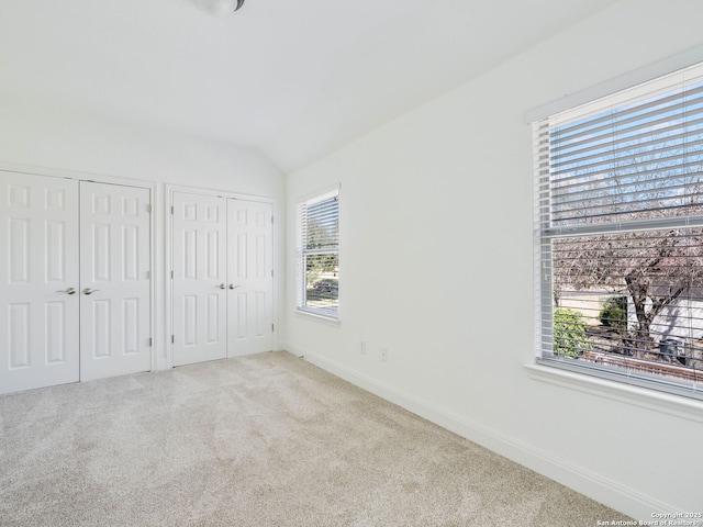 unfurnished bedroom featuring two closets, light carpet, and lofted ceiling