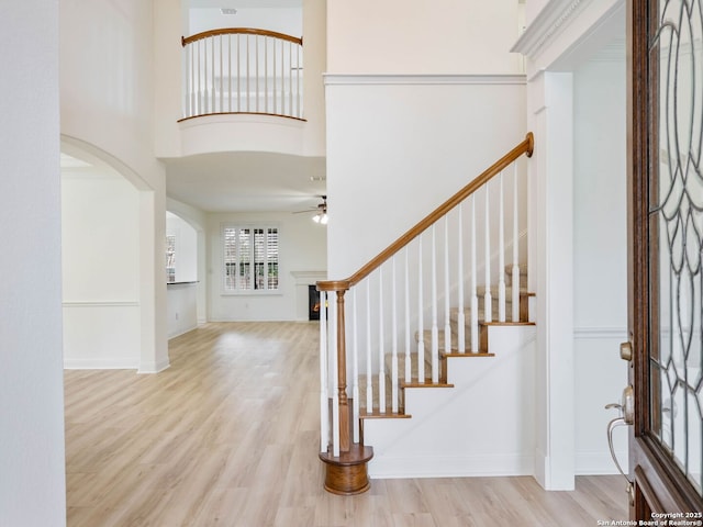 entryway with light wood-type flooring, ceiling fan, and a towering ceiling