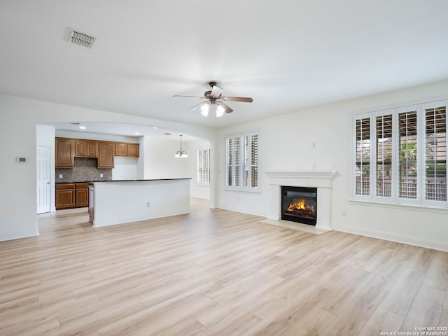 unfurnished living room featuring light wood-type flooring and ceiling fan with notable chandelier