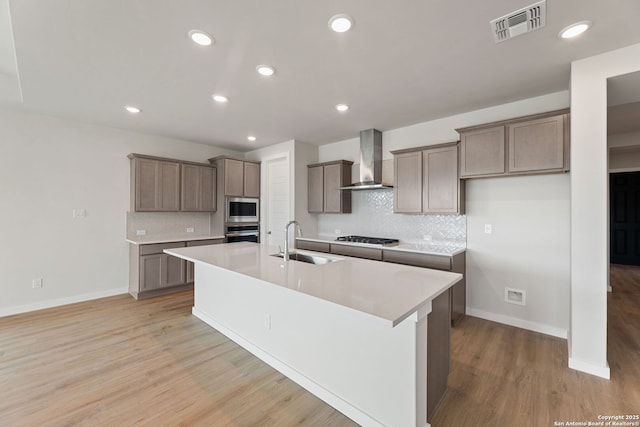 125 Connor Crk, San Antonio, TX 78253 - kitchen featuring wall chimney exhaust hood, appliances with stainless steel finishes, a sink, an island with sink, and light wood-style flooring