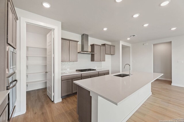125 Connor Crk, San Antonio, TX 78253 - kitchen featuring wall chimney exhaust hood, a sink, appliances with stainless steel finishes, light wood-style floors, and an island with sink
