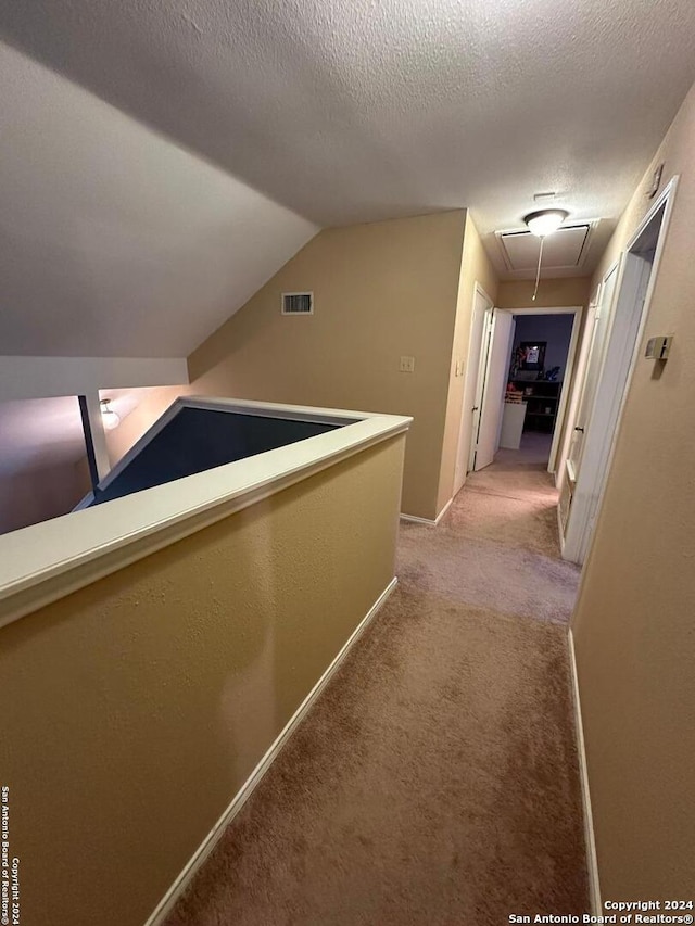 hall featuring light carpet, vaulted ceiling, and a textured ceiling