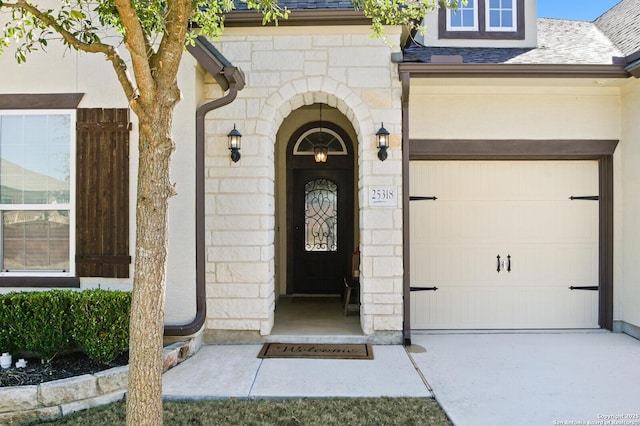 property entrance featuring a garage, stone siding, concrete driveway, and roof with shingles