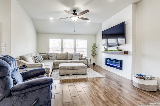 living room featuring hardwood / wood-style flooring, vaulted ceiling, a large fireplace, and ceiling fan