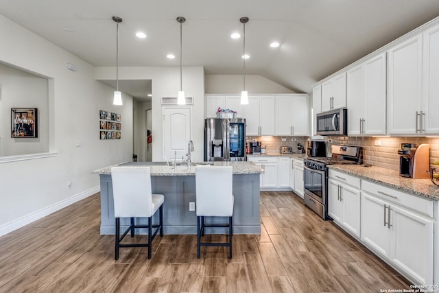 kitchen featuring a center island with sink, stainless steel appliances, light stone counters, white cabinets, and pendant lighting