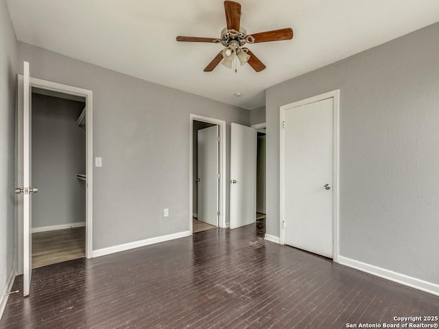 unfurnished bedroom with ceiling fan, dark wood-type flooring, a walk in closet, and a closet