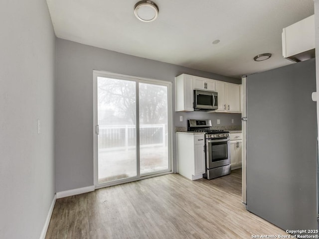 kitchen with appliances with stainless steel finishes, light wood-type flooring, white cabinetry, and light stone countertops