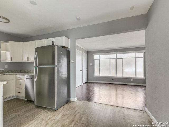 kitchen with white cabinets, light wood-type flooring, stainless steel appliances, and light stone counters