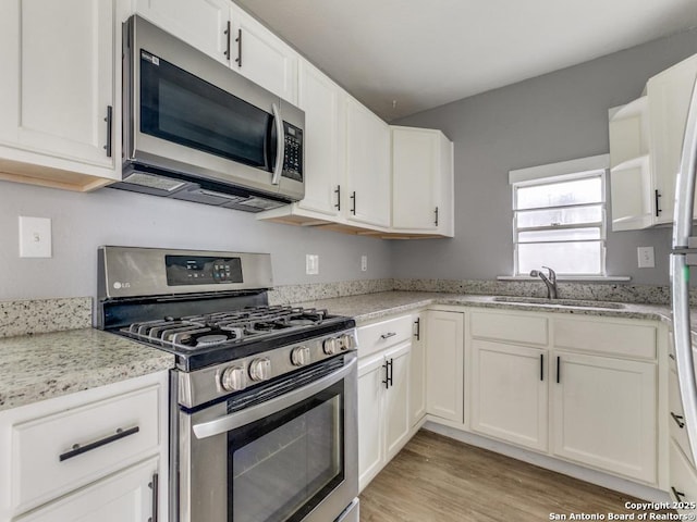 kitchen featuring sink, white cabinets, stainless steel appliances, and light stone counters