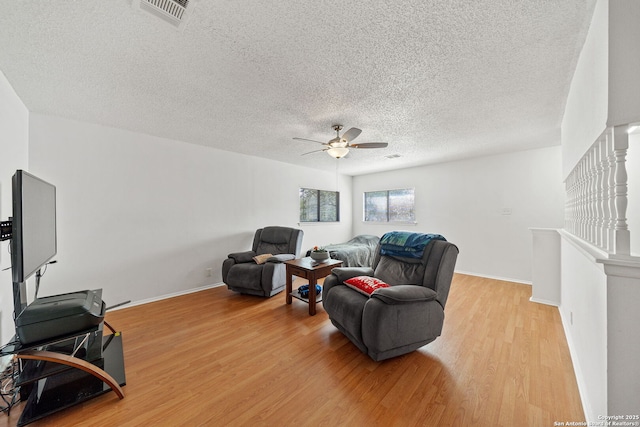 living room featuring light hardwood / wood-style flooring, ceiling fan, and a textured ceiling