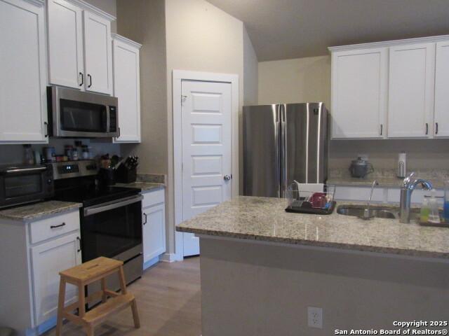 kitchen featuring stainless steel appliances, light hardwood / wood-style flooring, light stone countertops, sink, and white cabinets