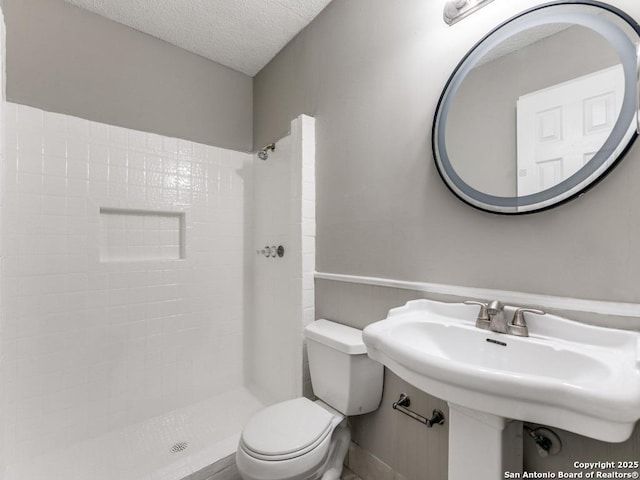 bathroom featuring a textured ceiling, toilet, and tiled shower