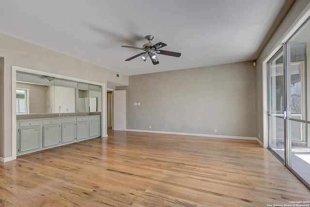 unfurnished living room with baseboards, a sink, a ceiling fan, and light wood-style floors