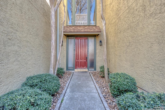 entrance to property featuring a shingled roof and stucco siding