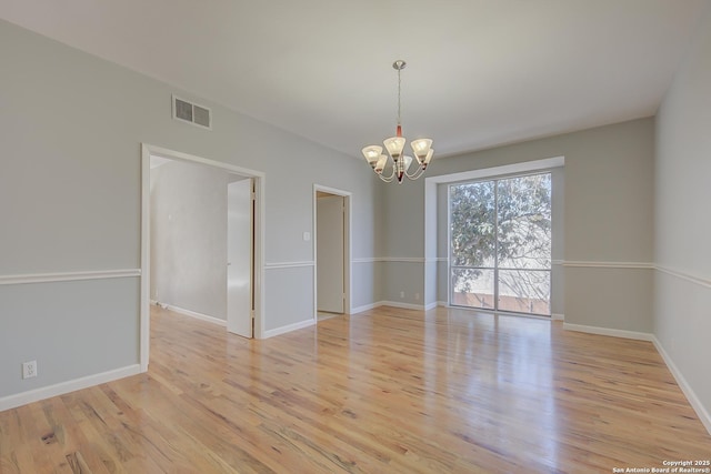 spare room featuring light wood-type flooring, baseboards, visible vents, and a chandelier