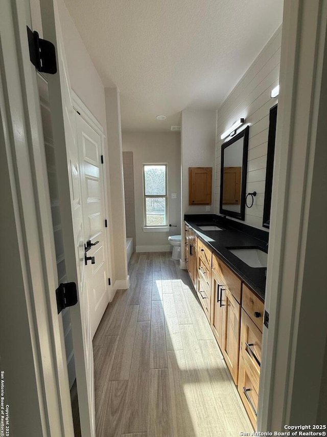 bathroom with toilet, a textured ceiling, hardwood / wood-style floors, vanity, and a bathtub