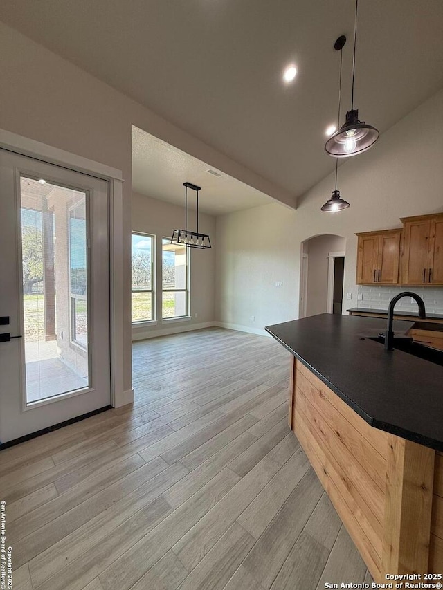 kitchen featuring light hardwood / wood-style flooring, decorative light fixtures, high vaulted ceiling, backsplash, and sink