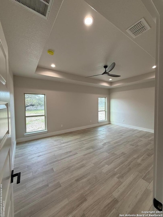 unfurnished room with a raised ceiling, light wood-type flooring, ceiling fan, and a textured ceiling