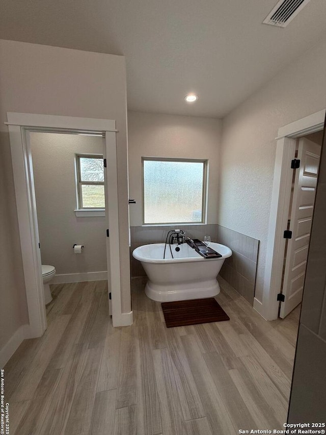 bathroom featuring a washtub, toilet, and hardwood / wood-style floors