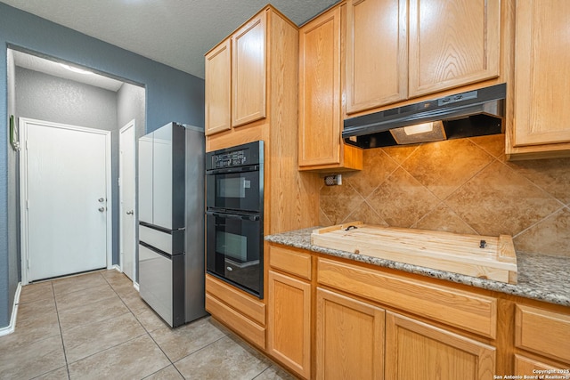 kitchen with black double oven, backsplash, fridge, light tile patterned flooring, and light stone countertops