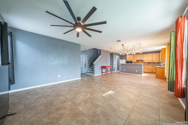 unfurnished living room featuring sink, light tile patterned flooring, and ceiling fan with notable chandelier